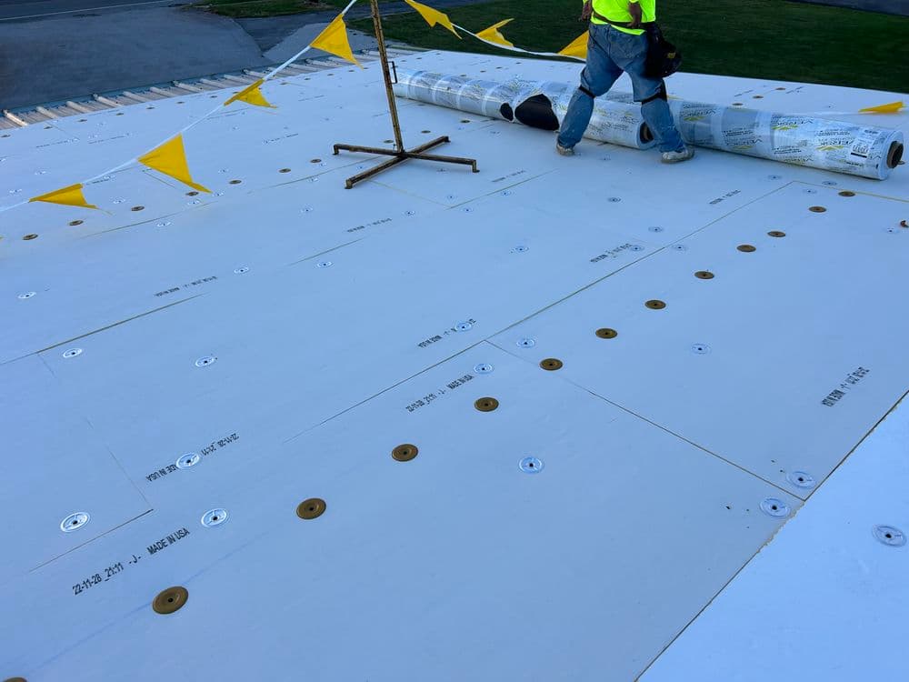 Worker installing roofing materials with yellow safety flags on a flat surface.
