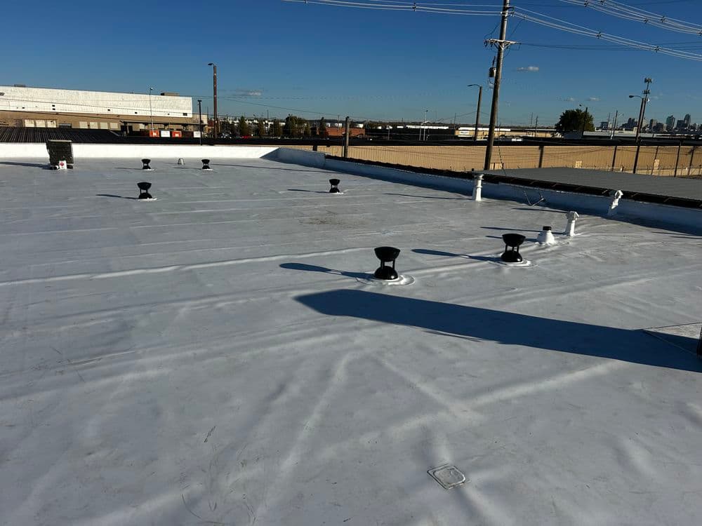 Flat commercial roof with ventilation pipes and clear sky in the background.