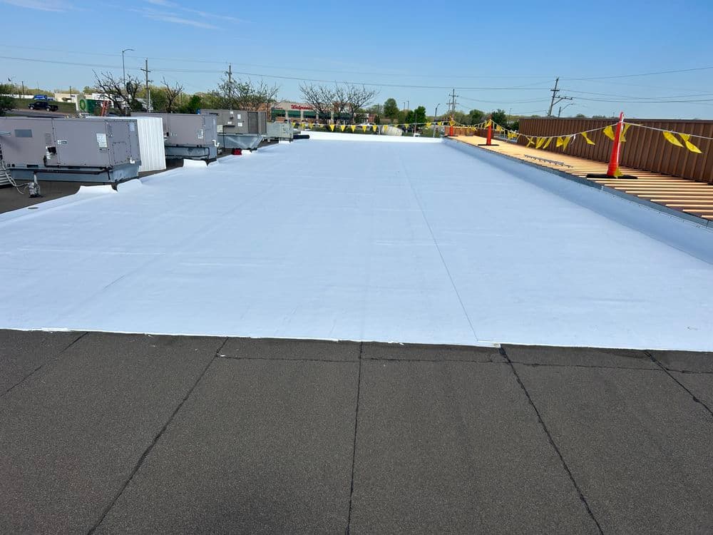 Flat commercial roof installation with white membrane, HVAC units, and safety barriers.