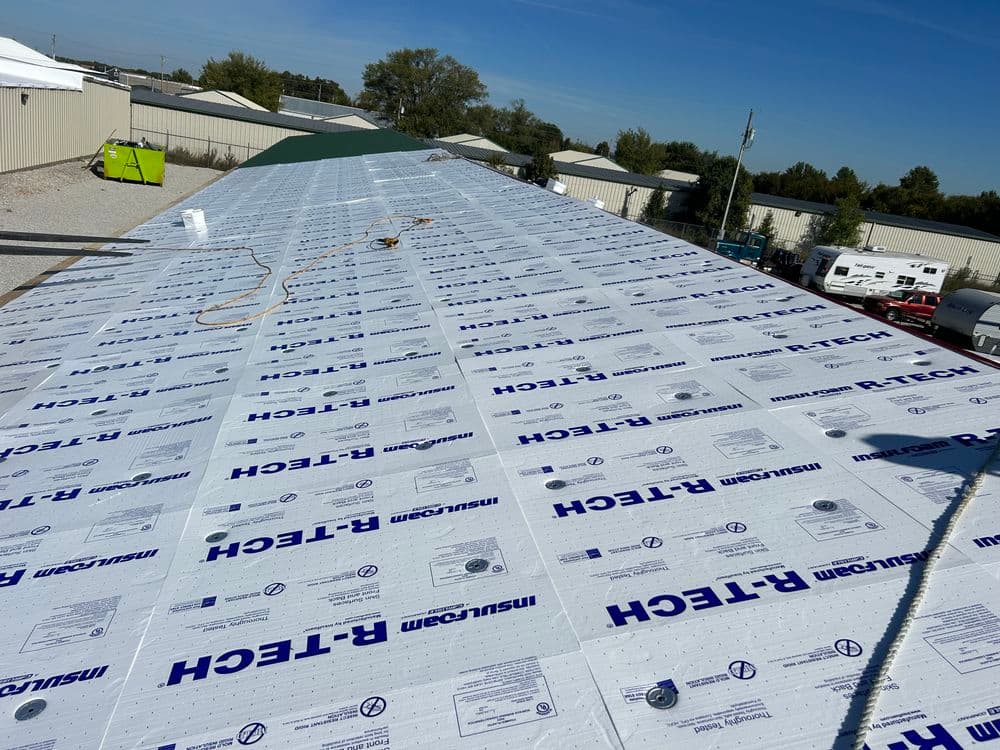 Roof installation with R-Tech insulation boards covering a building under clear blue sky.