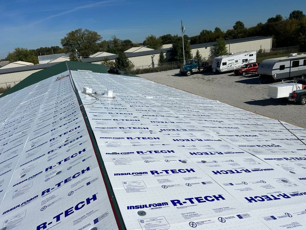 Installation of R-Tech insulation boards on a commercial roof under a clear blue sky.