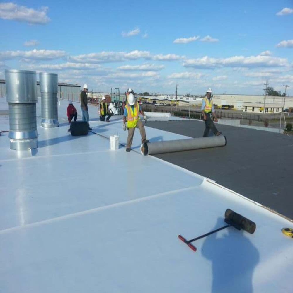 Construction workers installing roofing material on a commercial building rooftop.