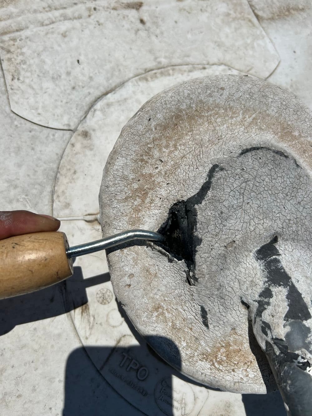Hand using a paint roller to apply black coating on a textured surface.