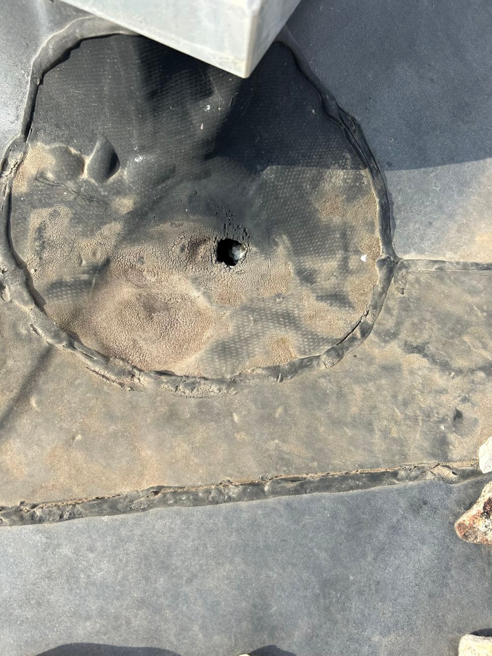 Damaged roofing material showing a hole surrounded by cracked surface, revealing wear.