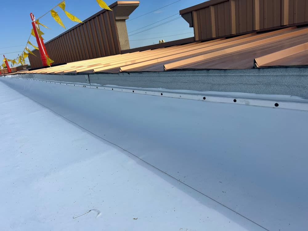 White membrane roof with metal edge and decorative flags in the background on a clear day.