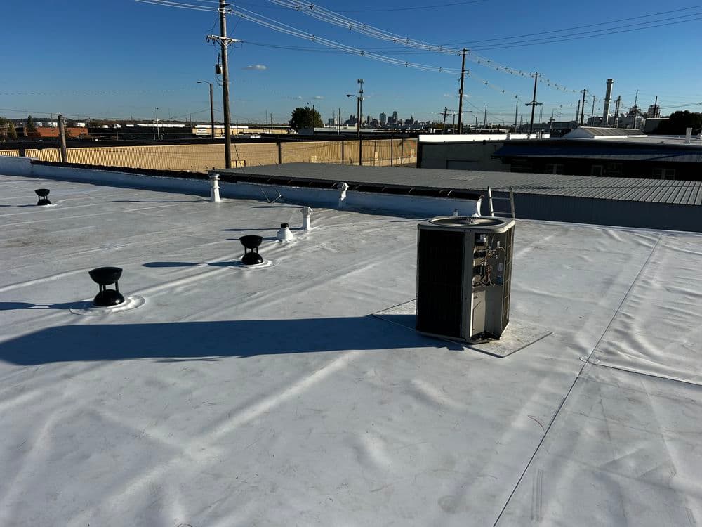 Flat commercial rooftop with HVAC unit and skyline in the background, clear blue sky.