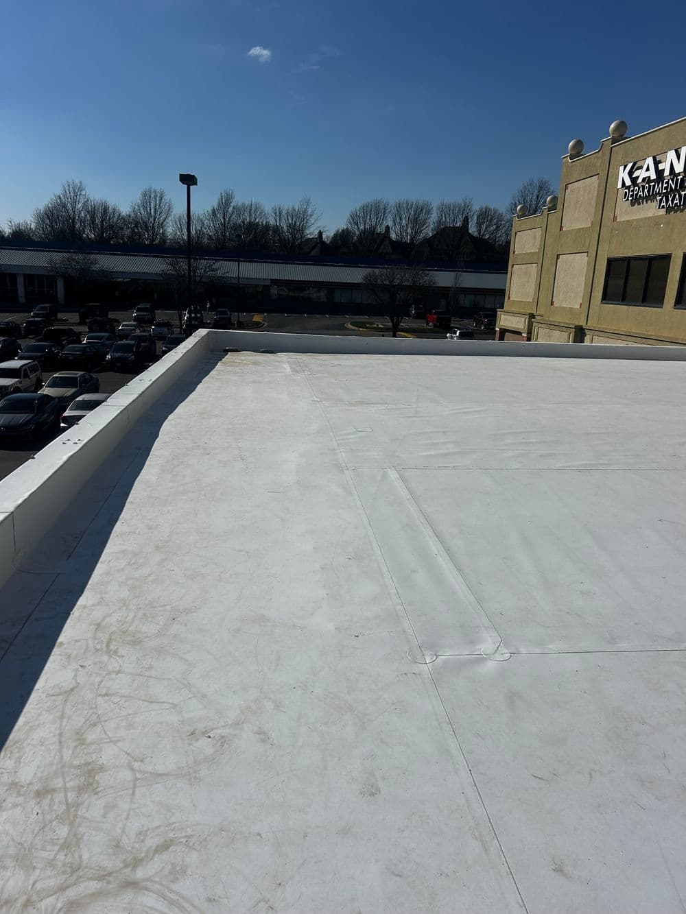 View of a commercial flat roof with a clear blue sky and shopping center in the background.