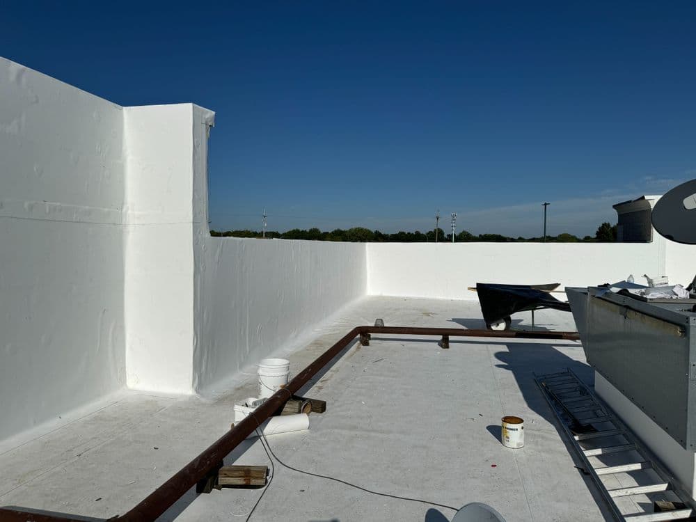 White commercial roof with a clear blue sky, featuring construction materials and tools.