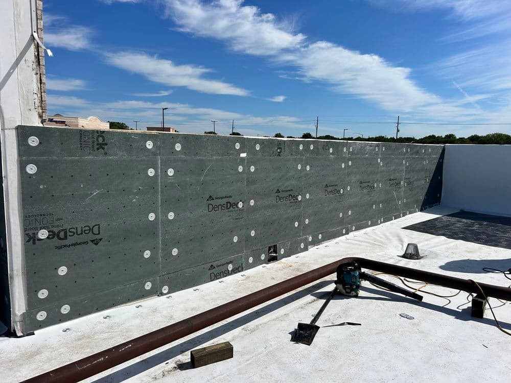 DensDeck roofing installation on a flat roof under a blue sky with construction tools.