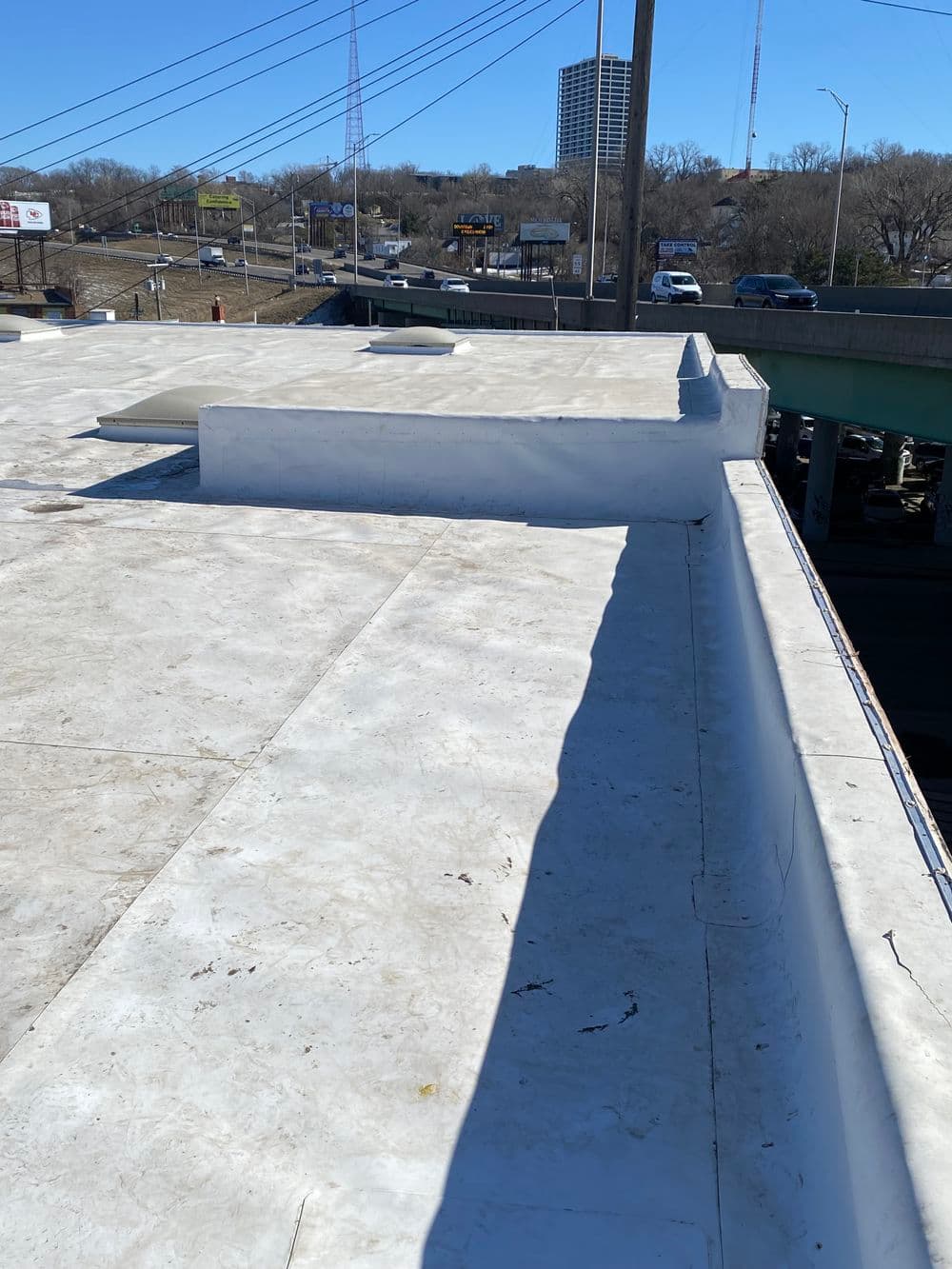 Flat rooftop view overlooking a busy street and buildings, with clear blue sky.