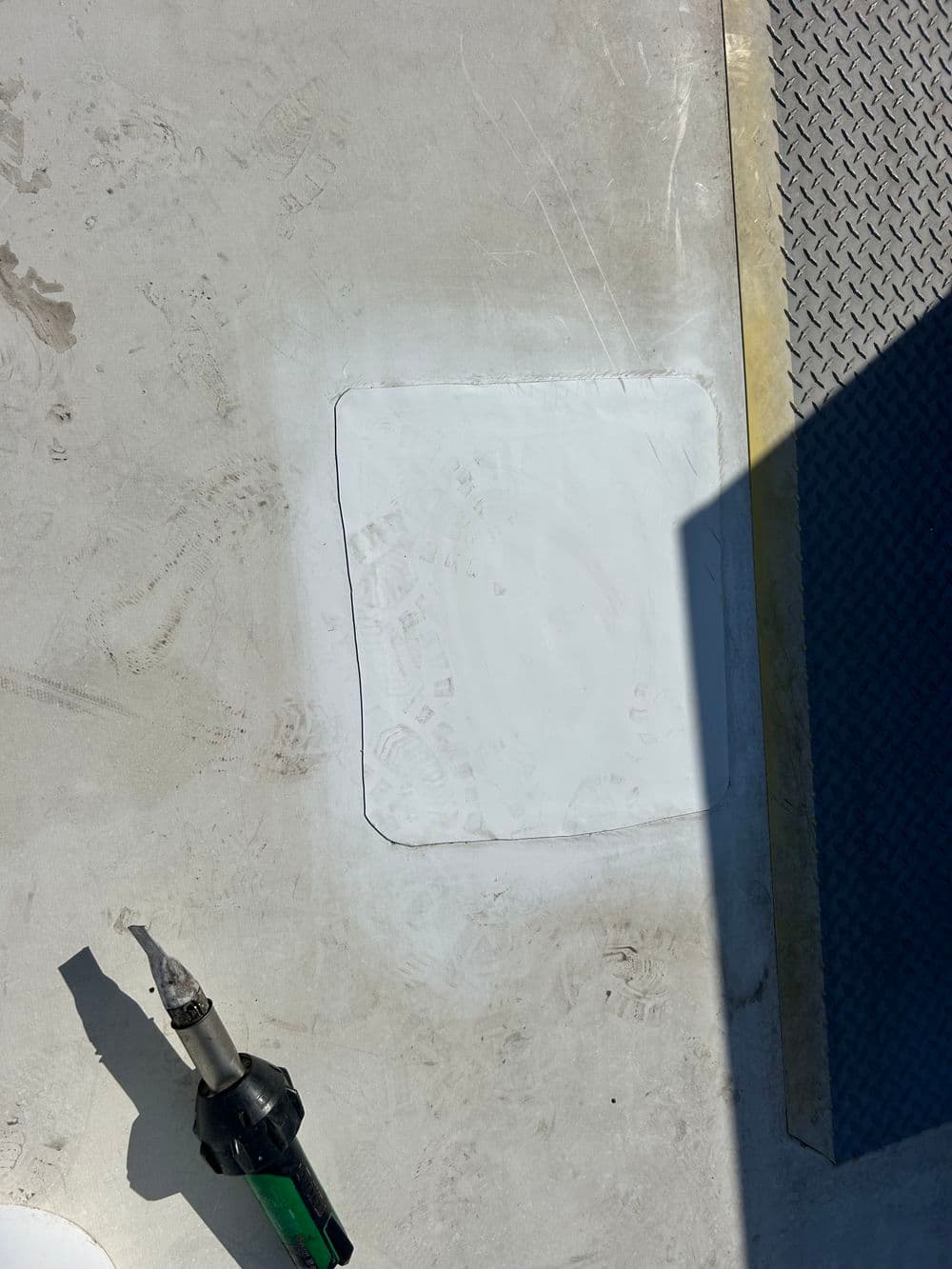Concrete surface repair with a fresh patch and repair tool nearby, sunlight casting a shadow.