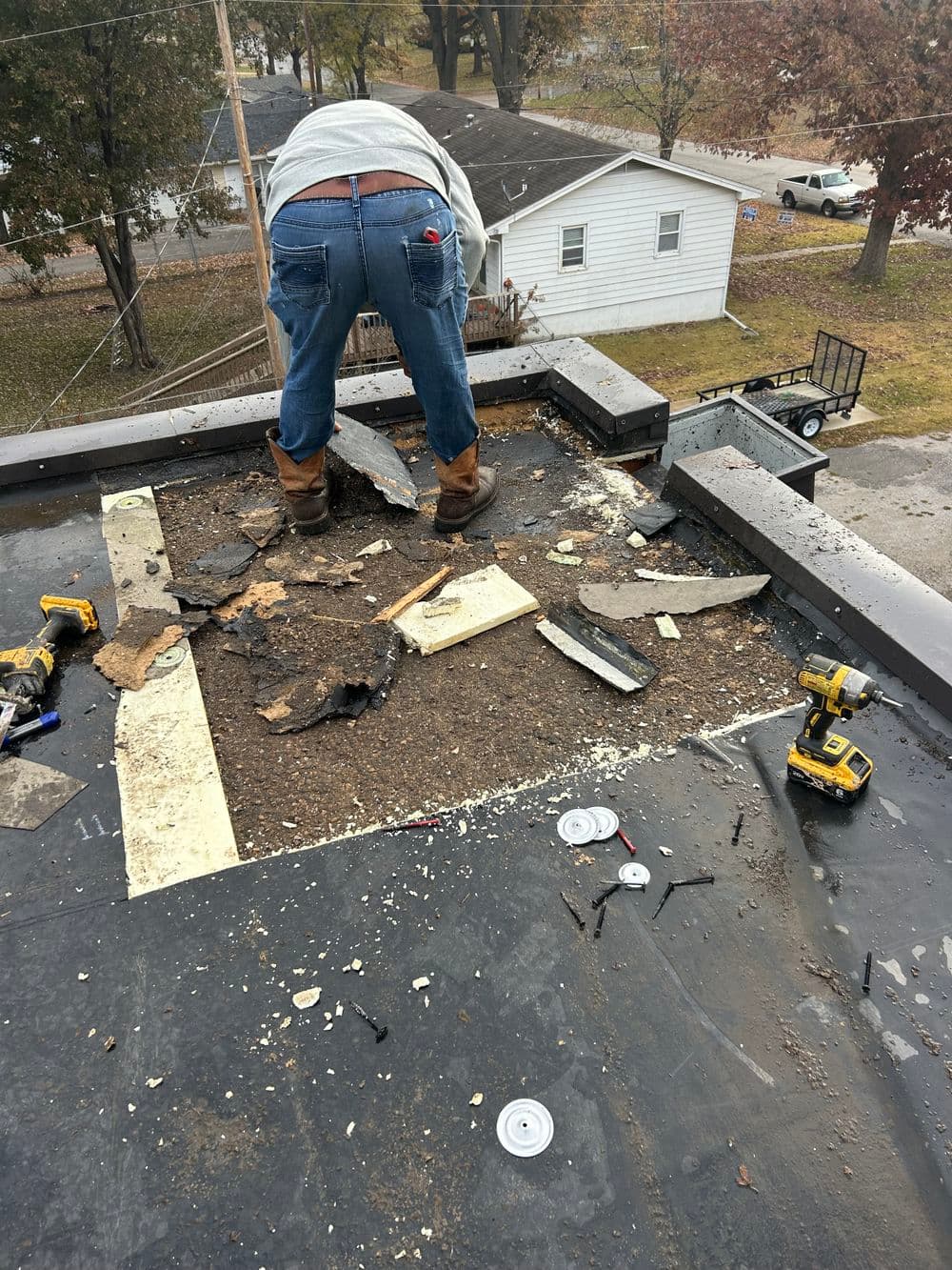 Roofer removing debris from a flat roof, tools and materials scattered around.