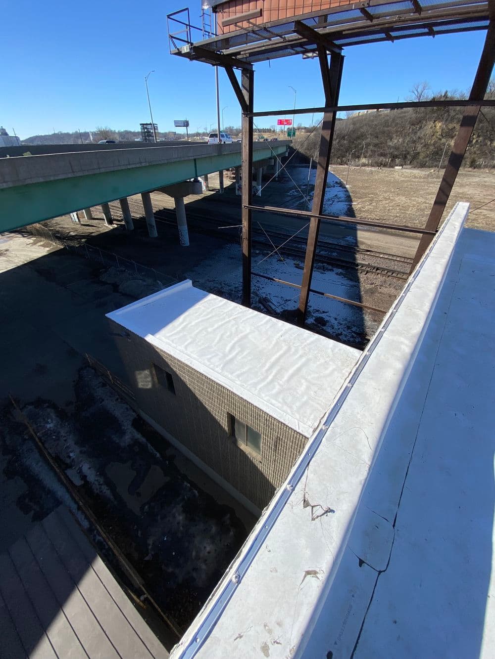 View of an industrial area with a rooftop, highway overpass, and railway tracks below.