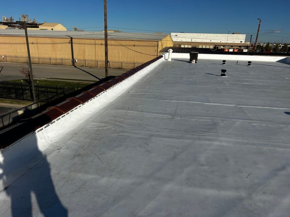 Flat commercial roof with white membrane and rooftop vents under clear blue sky.