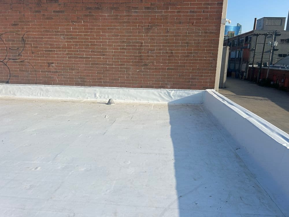 Flat white roofing on a commercial building with a brick wall backdrop and clear sky.