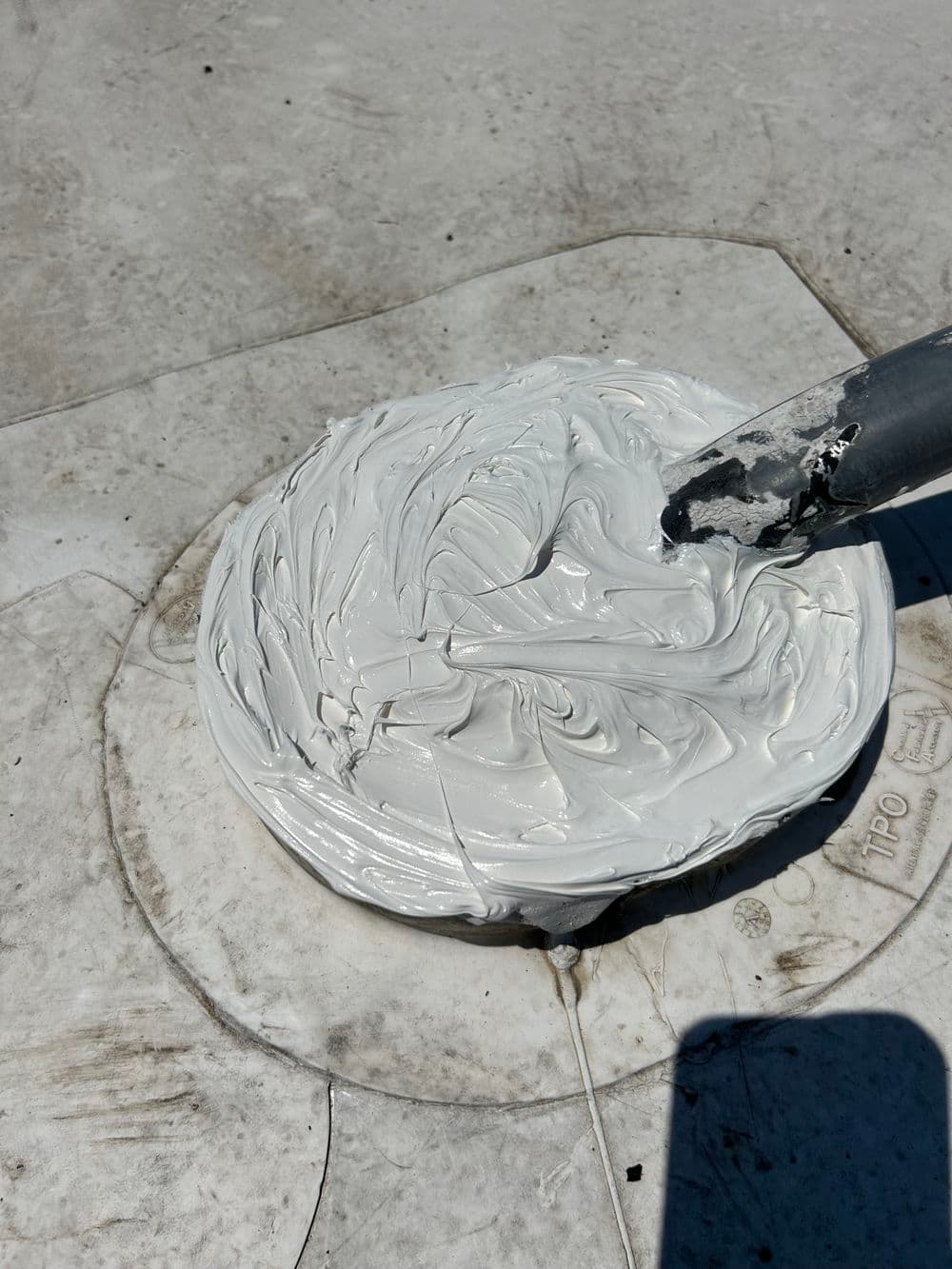 White adhesive paste being mixed on a surface with a spatula. Ideal for construction projects.
