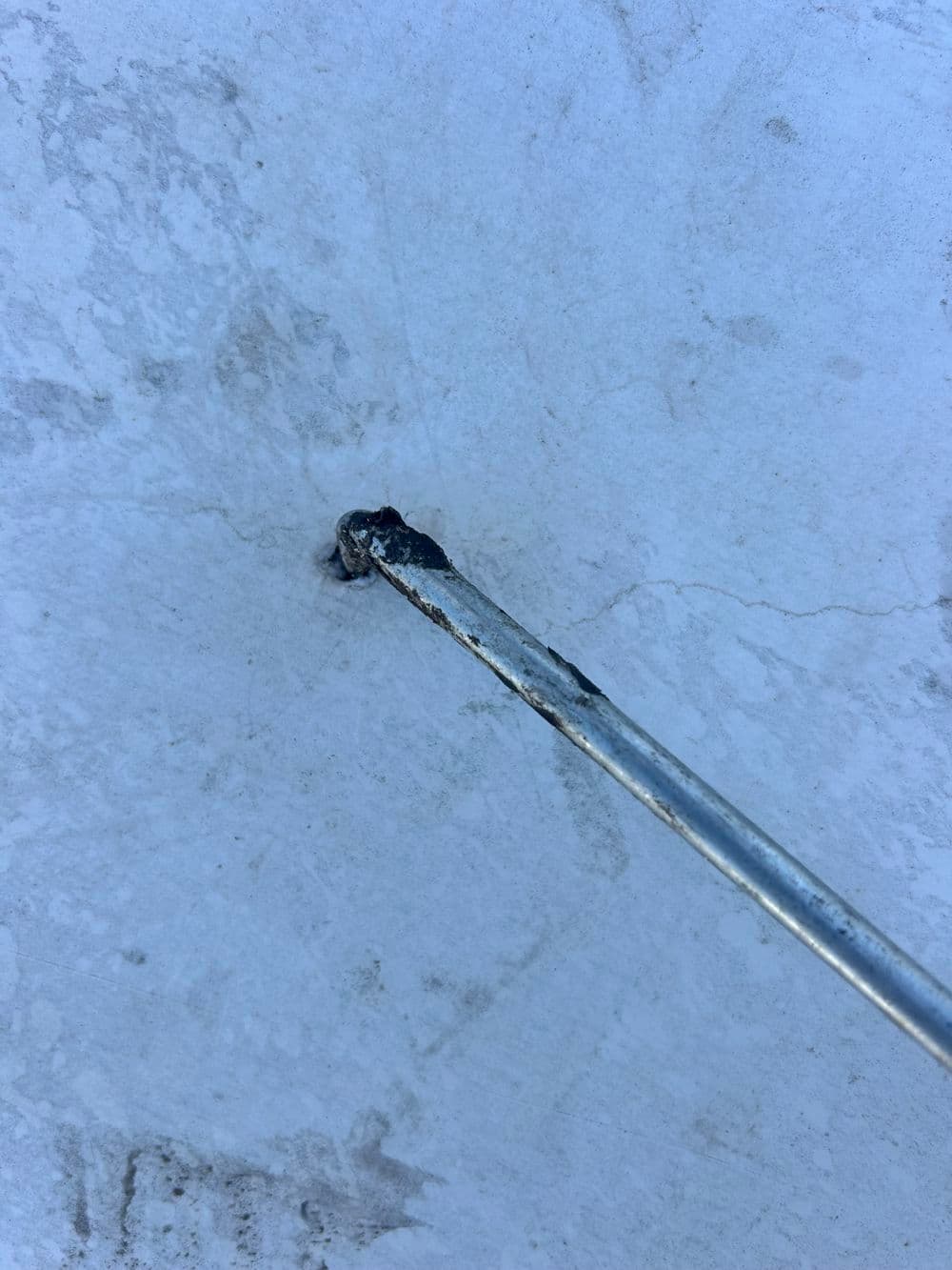 Metal rod inserted into a cracked white surface, showing signs of wear and damage.