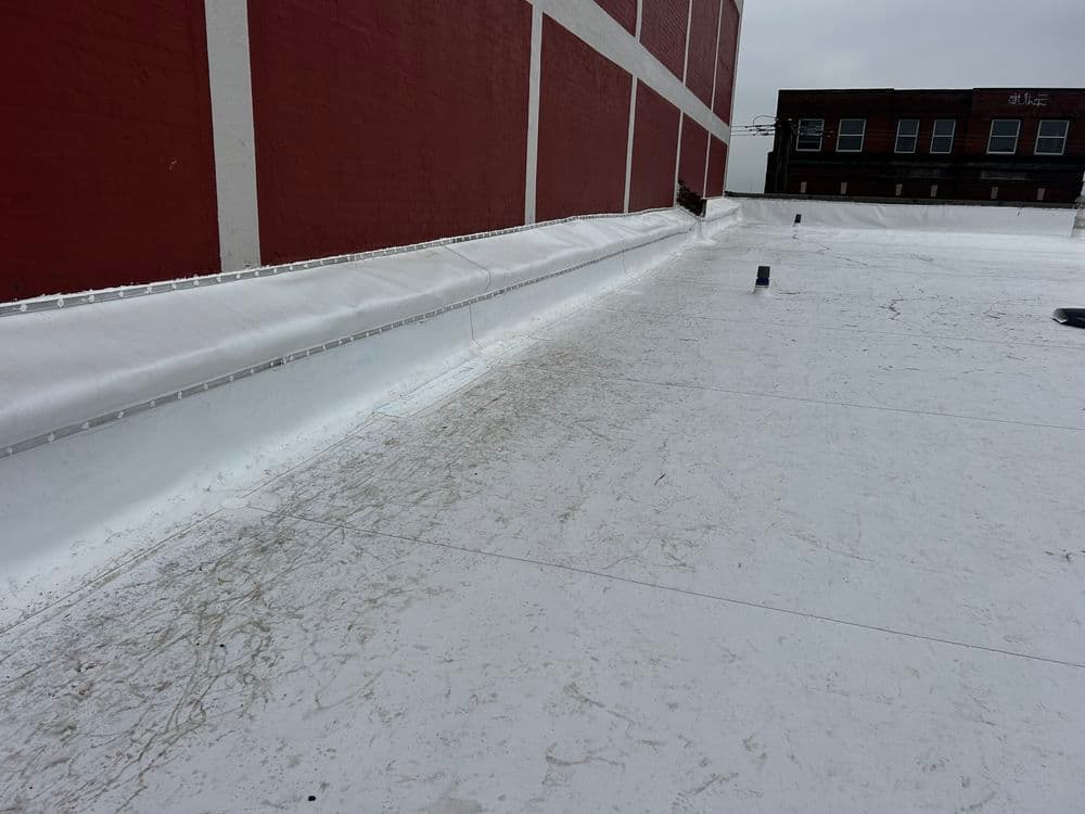 Flat white roofing membrane on a commercial building with red brick wall in background.