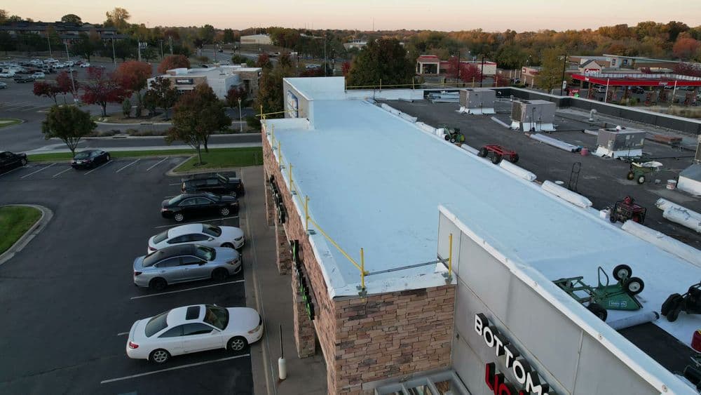 Aerial view of a flat roof with safety railings, surrounded by parking and commercial buildings.