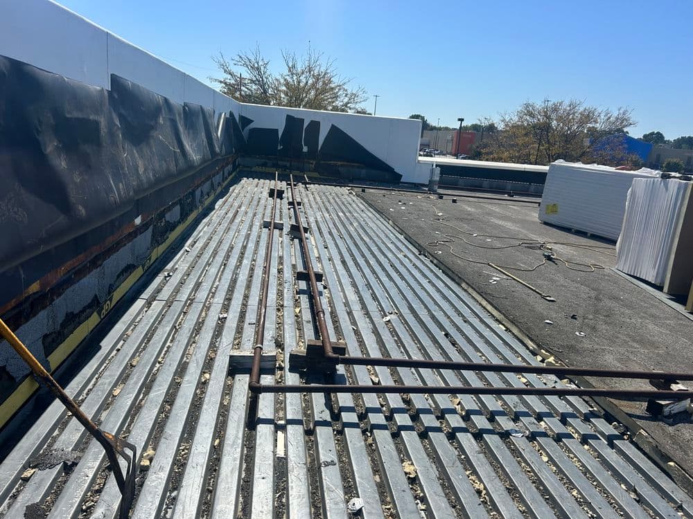 Roof construction site with metal panels and exposed insulation under a clear blue sky.