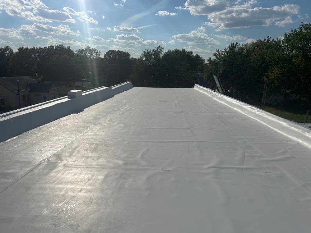 Flat rooftop with a white coating under a clear sky and scattered clouds.