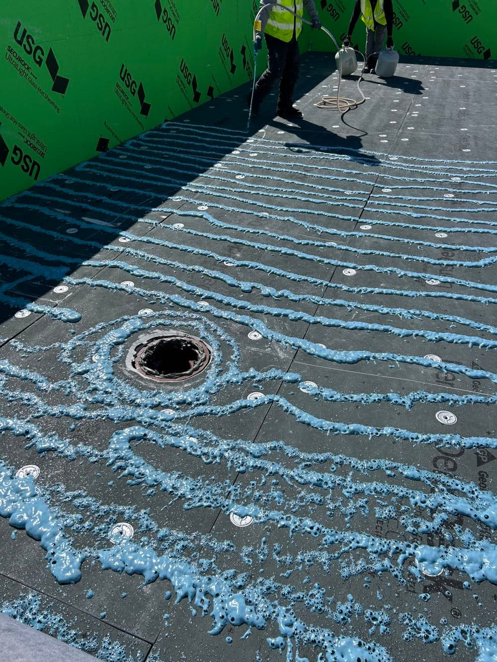 Workers applying waterproofing membrane with drain in construction area.