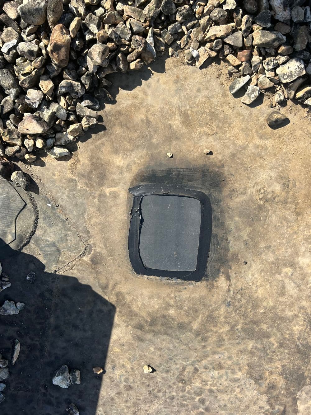 Black patch on a concrete surface surrounded by small gravel stones.
