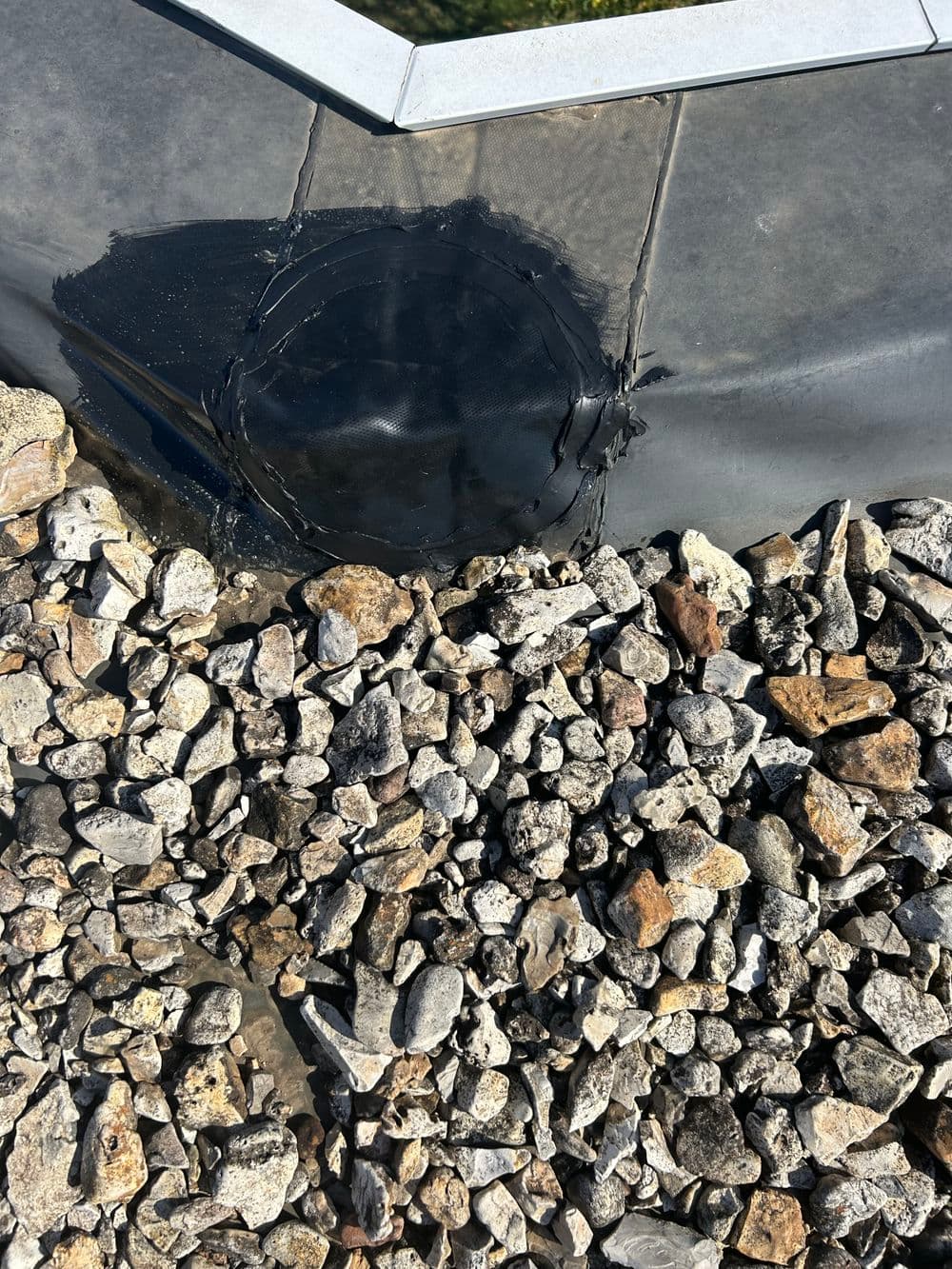 Roofing repair showing black sealant and rocky substrate around a damaged area.